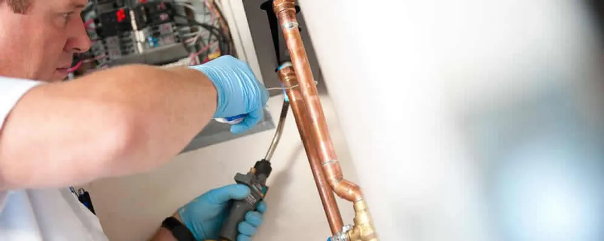 Water heater repair technician testing copper pipe connections and controls in Lexington, MA